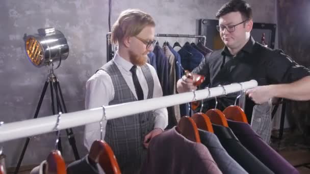 Покупки концепції. Продавець допомагає молодий чоловік вибрати костюм в магазині - Кадри, відео