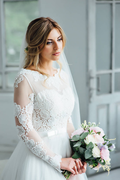 Beautiful bride in white wedding dress with a wedding bouquet standing near the wooden door - Foto, imagen