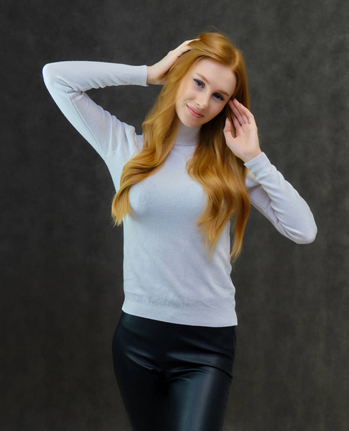 Concept portrait of a cute beautiful red-haired girl talking on a gray background in the studio. She is wearing a white sweater and shows different emotions in different poses. - Zdjęcie, obraz