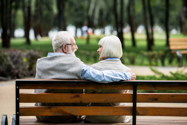 happy senior couple resting on wooden bench in park - Zdjęcie, obraz