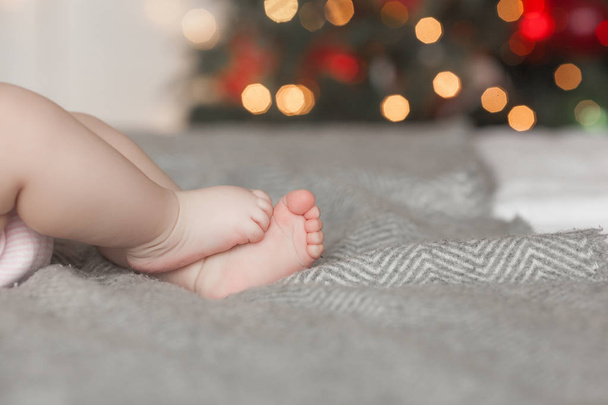 Vauvan jalat sängyllä. Taustalla tunnistamattomat lapsen pikkusormet. Pikkulapsen varpaat, joissa on vapaa tila
 - Valokuva, kuva