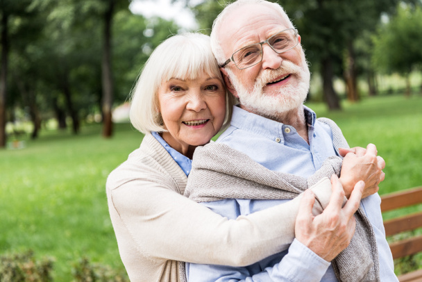 happy senior woman hugging smiling husband in park - Photo, Image