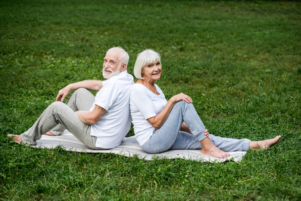 smiling senior couple relaxing on yoga mats in park - Zdjęcie, obraz