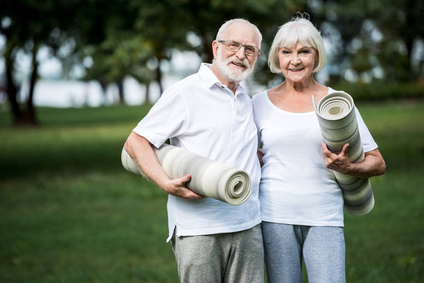 smiling senior couple embracing while holding fitness mats - Foto, imagen