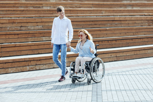 Woman in wheelchair with boyfriend strolling in city summer park - Foto, imagen