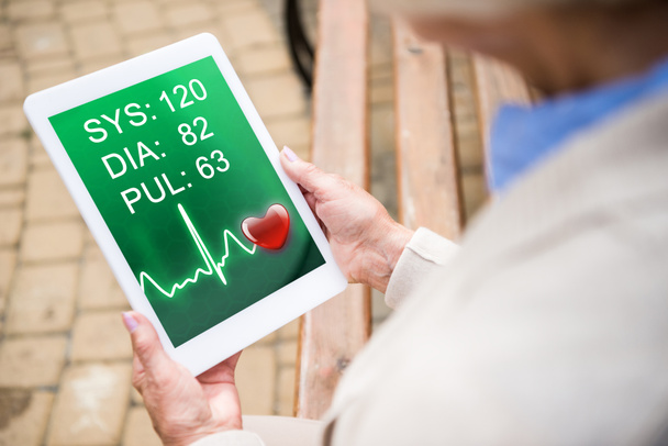 Selektive Fokussierung der Seniorin mittels digitaler Tabelle mit Herzfrequenz auf dem Bildschirm - Foto, Bild