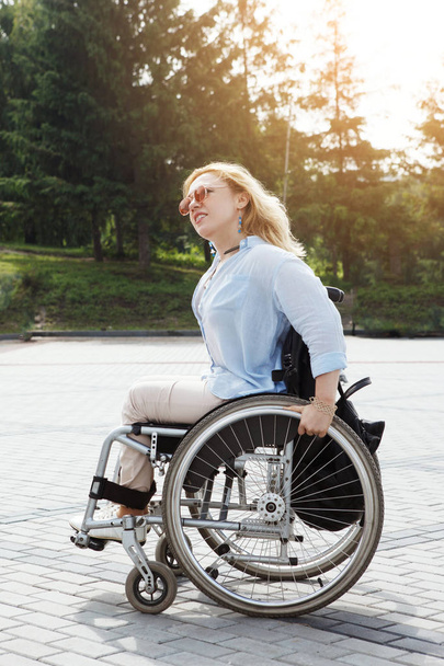 Mulher montando cadeira de rodas na estrada no parque de verão da cidade
 - Foto, Imagem