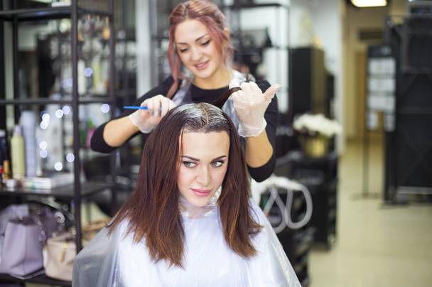 プロの女性美容師デザインの美容院、彼女の髪を持つ女性で女性のお客様に色を適用します。プロセスで着色染毛剤  - 写真・画像