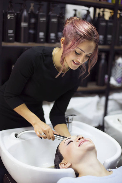 Nádherná veselá mladá žena těší masáž hlavy a zároveň si myje vlasy profesionálním kadeřníkem. Beauty care, hairstyling, fashion, lifestyle glamour concept - Fotografie, Obrázek