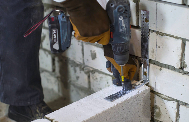 builder screwing joining clamp in aerated concrete block with electric drill - Foto, Imagen