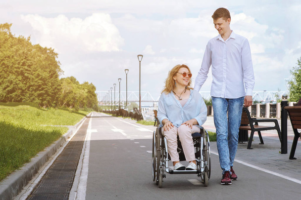 Женщина в инвалидной коляске с бойфрендом прогуливается в городском летнем парке
 - Фото, изображение