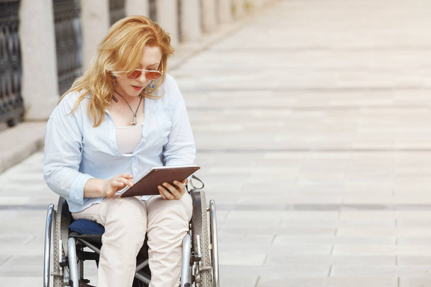 Женщина на инвалидной коляске с помощью смартфона в летнем городском парке
 - Фото, изображение