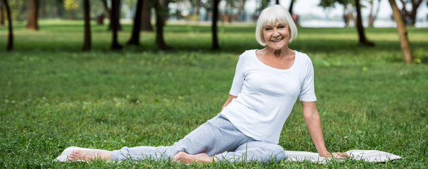 smiling senior woman relaxing on yoga mat on green lawn - Фото, изображение