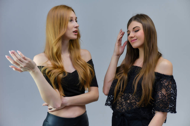 A concept portrait of two cute beautiful girls talking on a gray background in the studio are standing in front of the camera. They show different emotions in different poses. - Foto, imagen