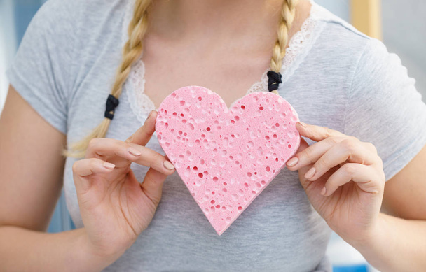 Woman having two cute braids on blonde hair holding pink sponge in heart shape. Haircare and hairstyling concept. - Valokuva, kuva