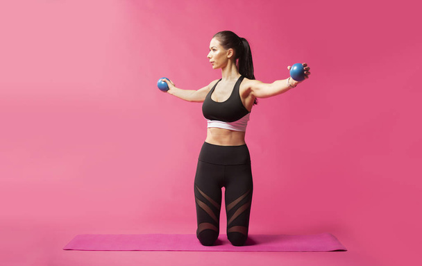 Long haired beautiful pilates or yoga athlete does a graceful pose while wearing a tight sports outfit against a pink background in a studio - Photo, Image