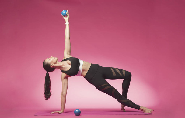 Long haired beautiful pilates or yoga athlete does a graceful pose while wearing a tight sports outfit against a pink background in a studio - Foto, imagen