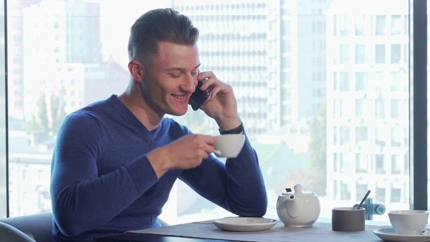 Handsome man enjoying drinking tea and talking on the phone at the restaurant - Fotoğraf, Görsel