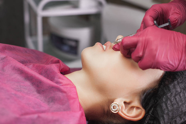 Procedure van lipvergroting in de schoonheidssalon. Cosmetoloog die hyaluronzuur injecteert om de lippen te stimuleren. Vrouw in de kosmetologische salon - Foto, afbeelding