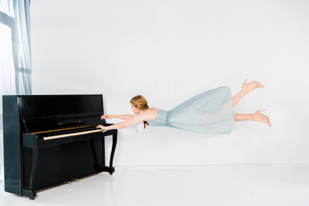 floating girl in blue dress playing black piano on white background - Фото, зображення