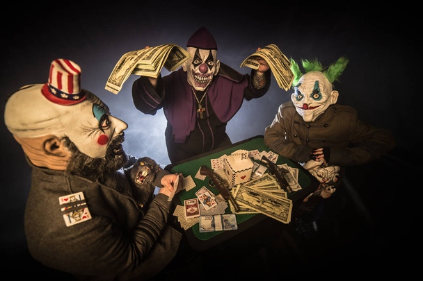 payasos asustadizos sentados en la mesa y jugando al póquer por dinero en el casino, sacerdote sosteniendo efectivo
 - Foto, imagen