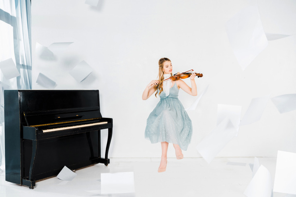 floating girl in blue dress playing violin with sheets of paper in air  - Fotografie, Obrázek