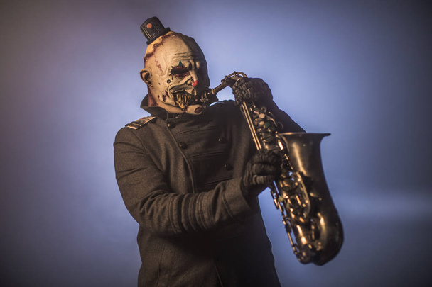 scary clown posing with saxophone against dark background - Fotó, kép