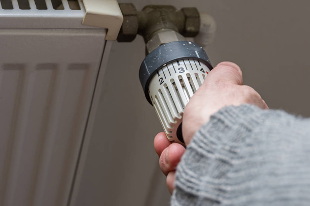 Male hand changing temperature on radiator. Heating season. Heating season. Savings in the bill. Saving Energy Concept. - Photo, Image