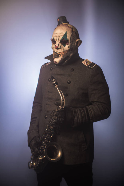 scary clown posing with saxophone against dark background - Foto, Imagem