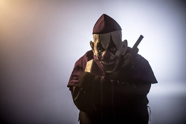 Dark priest in scary clown mask posing with money and gun against grey background - Fotoğraf, Görsel