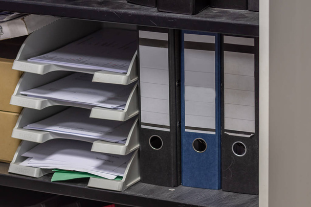 um armário de arquivos cinza com bandeja de documentos, ligantes de anel preto e azul em um fundo preto usado
 - Foto, Imagem