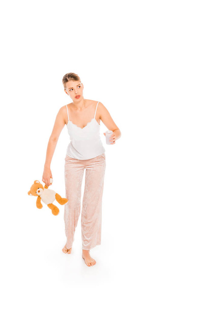 girl in pyjamas holding teddy bear and glass isolated on white  - Zdjęcie, obraz
