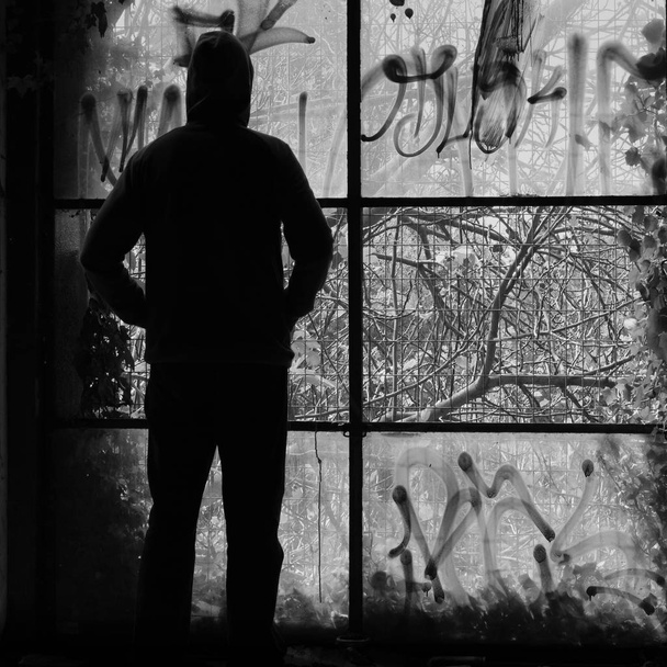Чоловік дивиться через зламані вікна покинутої будівлі. Чорно-білий
. - Фото, зображення