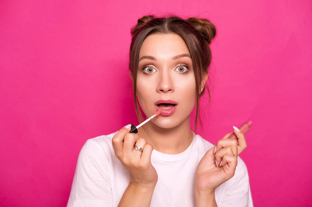 Sexy woman with stylish hairstyle in white t-shirt on a pink background applying make up, making amazed emotions - Foto, afbeelding