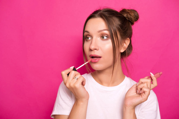 Sexy woman with stylish hairstyle in white t-shirt on a pink background applying make up, making amazed emotions - Photo, image