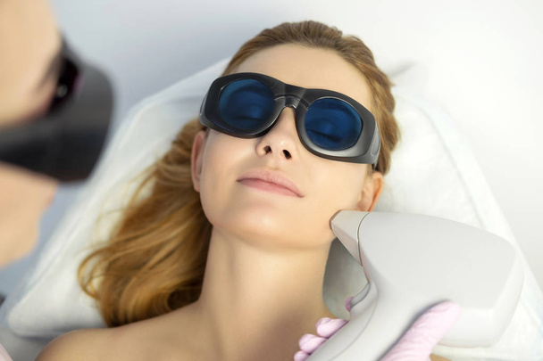 Женщина-косметолог удаляет волосы с тела клиентки с помощью лазерного эпилятора. Они в спа-центре
. - Фото, изображение
