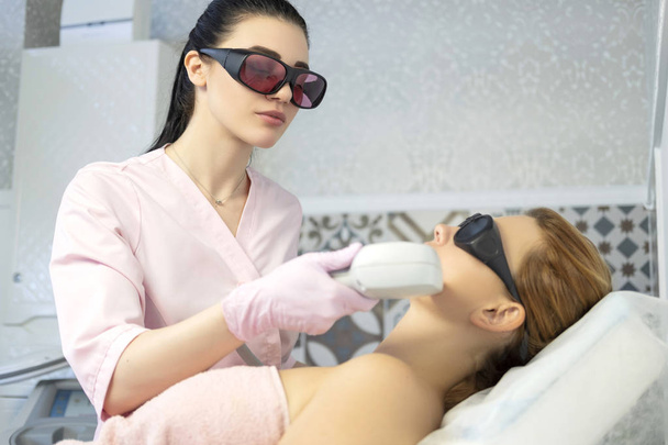 Woman doctor cosmetologist removing hair from a woman client body using laser epilator. They in a spa center. - Photo, Image
