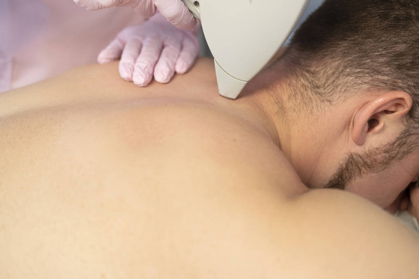 Mujer médico cosmetólogo quitando el cabello de un cuerpo de hombre usando depilador láser. Están en un centro de spa
. - Foto, imagen