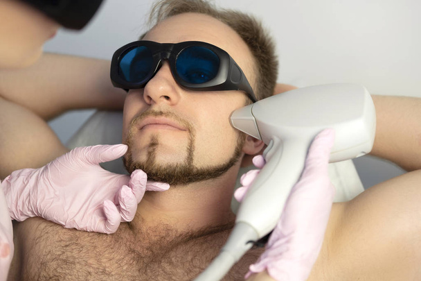 Женщина-косметолог удаляет волосы из тела мужчины с помощью лазерного эпилятора. Они в спа-центре
. - Фото, изображение