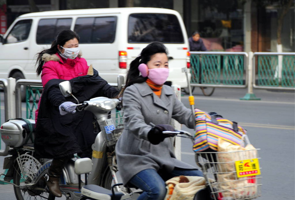 Chinese cyclists wearing masks drive their electric bikes on a street in Huaian city, east Chinas Jiangsu province, 4 December 2008 - Foto, imagen