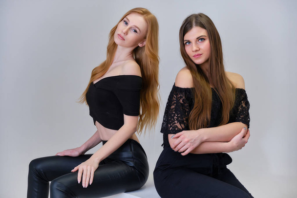 Concept portrait of two cute beautiful girls talking on a gray background in the studio sitting on the cubes in front of the camera. They show different emotions in different poses. - Valokuva, kuva