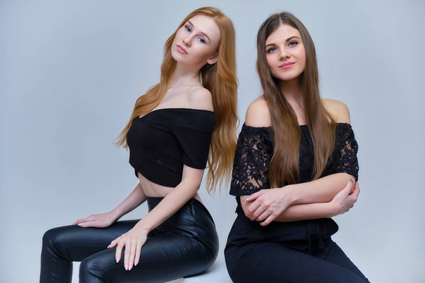 Concept portrait of two cute beautiful girls talking on a gray background in the studio sitting on the cubes in front of the camera. They show different emotions in different poses. - Valokuva, kuva