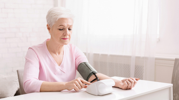 Starsza kobieta mierzy ciśnienie krwi w domu. - Zdjęcie, obraz