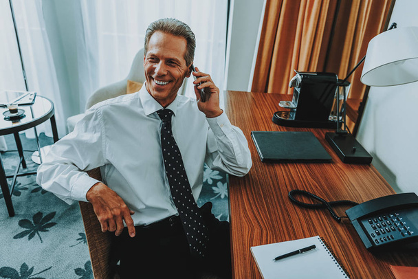 Delighted businessman talking on the phone while sitting at the table - Photo, image