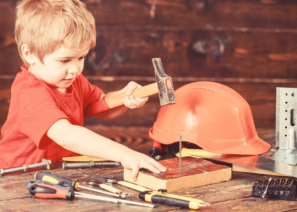 Toddler on busy face plays with hammer tool at home in workshop. Handcrafting concept. Kid boy play as handyman. Child cute and adorable playing as builder or repairer, repairing or handcrafting - Foto, Imagem