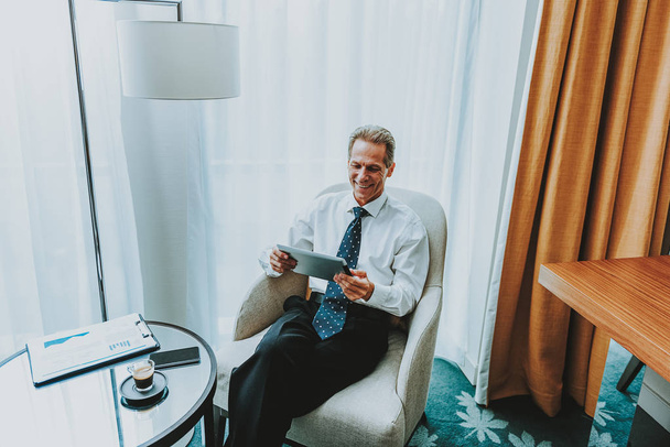 Positive businessman using tablet while sitting in the armchair - Fotó, kép