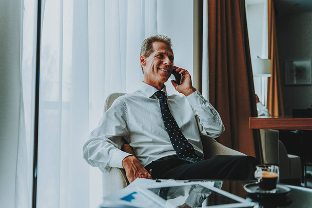 Waist up of positive businessman talking on the phone in armchair - Fotoğraf, Görsel