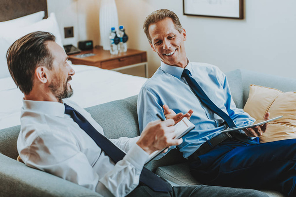 Waist up of two friendly businessmen smiling while sitting on the sofa - Photo, Image
