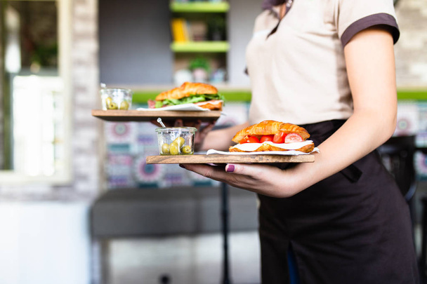 Vrouwelijke serveerster is het dragen van twee platen met broodjes. - Foto, afbeelding