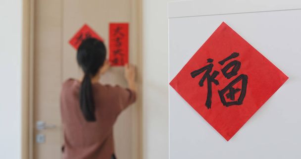 Frau klebt rote Kalligraphie auf die Tür, die zu Hause das chinesische Neujahrswort ziert, bedeutet Glück - Foto, Bild